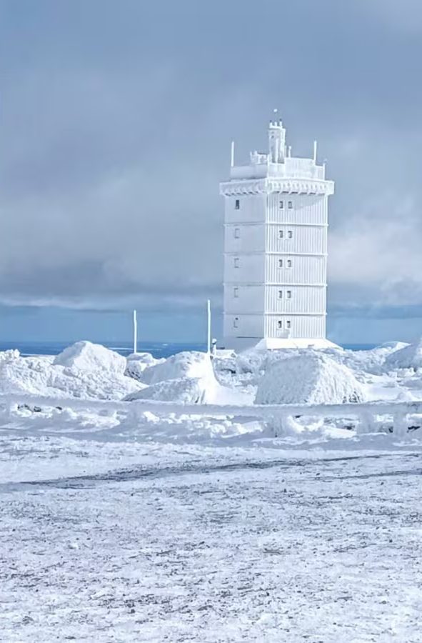 Brocken - Wetterstation Ein hoher, weißer Turm steht in einer verschneiten, winterlichen Landschaft.